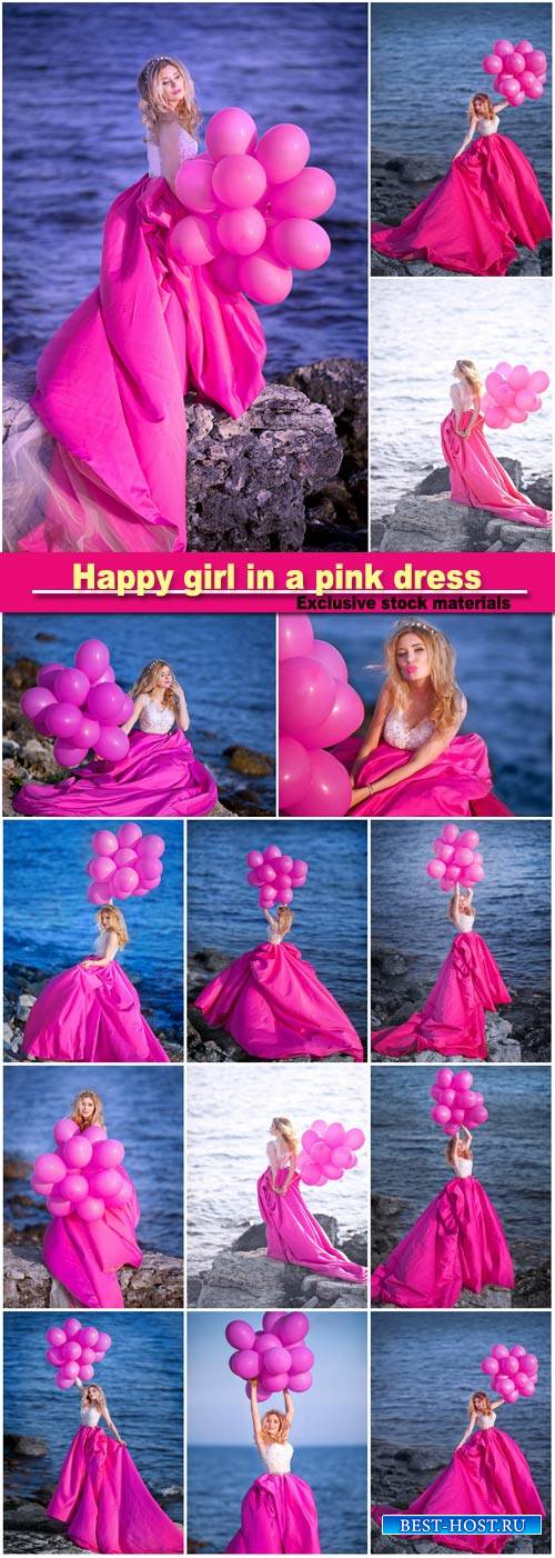 Happy girl in a pink dress with balloons is standing on the background of the waterfront
